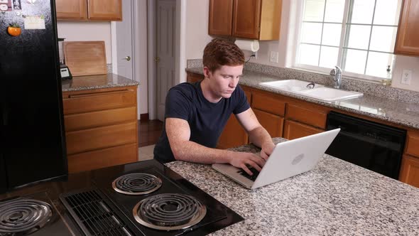 Young man working on laptop computer in kitchen at home