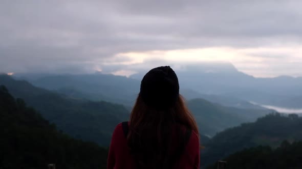 Slow motion blurred of a female traveler looking at a beautiful mountains view on foggy day