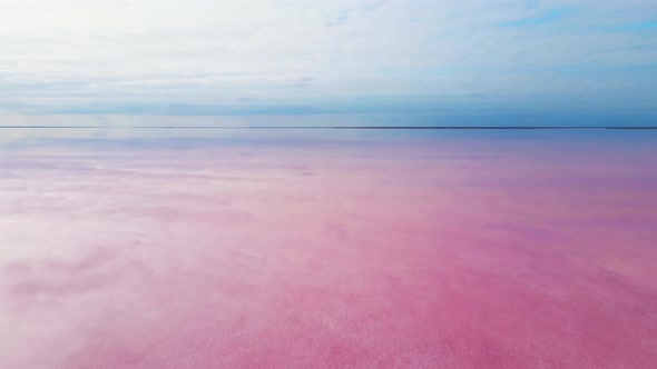 Smooth Surface of Colorful Pink Lake at Cloudy Sunrise with Wind Farm on Background alt