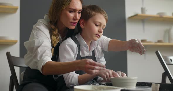 Happy Young Woman and Cute Child Boy Making Earthenware on Spinning Pottery Wheel in Workshop alt