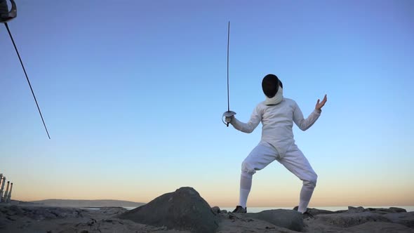 A man and woman fencing on the beach. alt