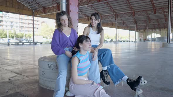 Three Girls Sit in Roller Skates and Talk As One Fixes Another’s Hair alt