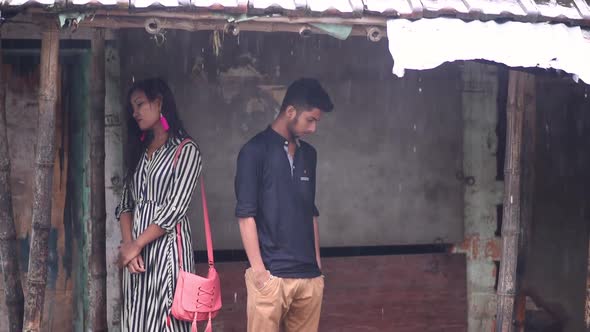 Annoyed and angry Asian couple stuck in rain under shade alt