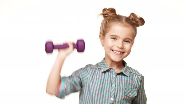 Small Active Caucasian Kid Girl in Plaid Shirt and Hair Buns Pushing Up Purple Dumbbell Smiling and alt