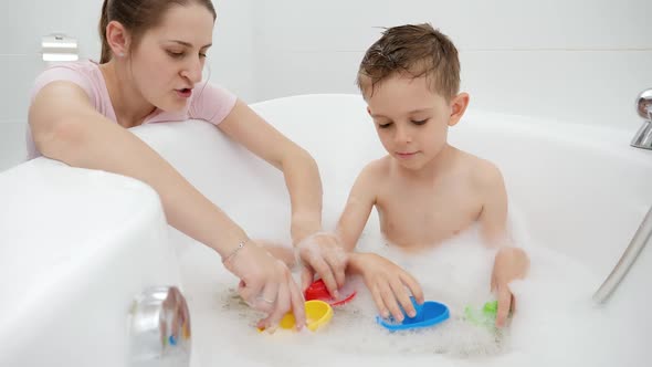 Smiling Mother Playing Toy Boats and Ships with Her Son Washing in Bath alt