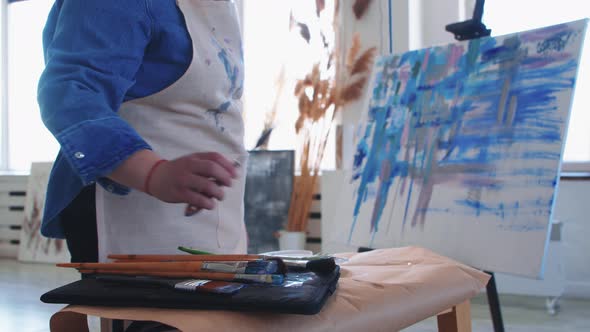 A Woman Paint Artist Taking a Brush and Drawing a Colorful Mostly Blue Painting on a Canvas alt