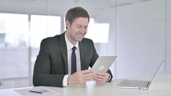 Middle Aged Businessman Doing Video Chat on Tablet in Office alt