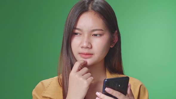 Close Up Of Young Asian Woman Use Phone And Thinking And Eyes Wide Open In Green Screen Studio alt