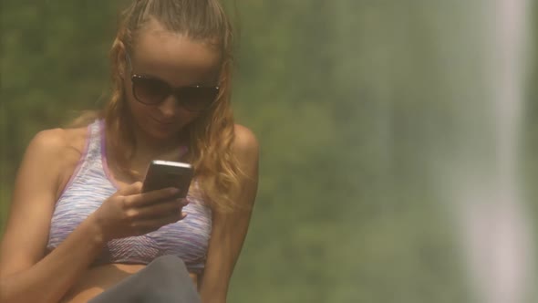 Blonde Lady in Sunglasses Texts Sms By Waterfall Closeup alt