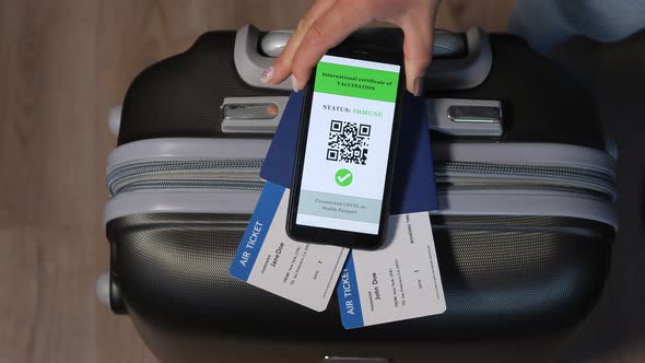Mobile Phone with a Digital Vaccination Certificate Near Passport and Suitcase alt
