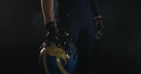 American Football Sportsman Player Holding a Helmet in His Hand on Black Background