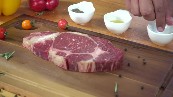 Chef cook season fresh chunk of deli piece of beef with sea salt and grounded spicy peppers.