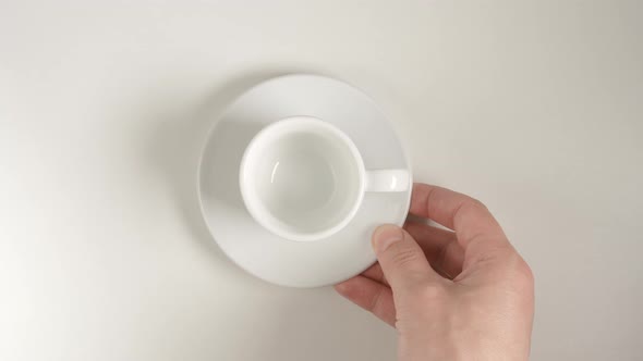 Top View: Human Hand Puts A White Coffee Cup On A White Table