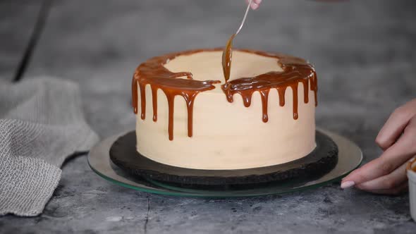 Closeup of a Pastry Chef Pouring Liquid Caramel Sauce From a Spoon on a White Cream Sponge Cake