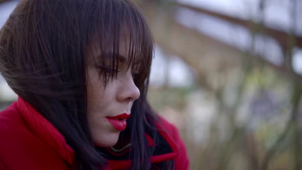 Portrait of a Brunette with Bright Lipstick and Piercings on Her Face. She's Wearing a Red Jacket alt
