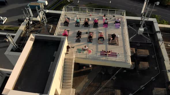A Group of People Do Yoga, Stretching and Meditation Outdoors on the Roof at Sunset alt