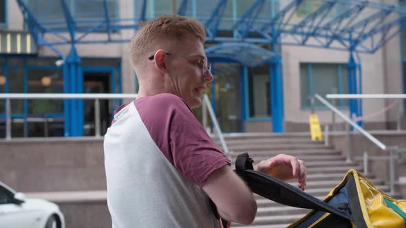 Young Male Courier Taking Off Yellow Insulated Food Delivery Backpack Stretching Muscles alt