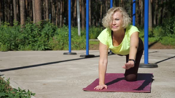 Young Pensioner Does Pilates on Mat on Park Sports Ground alt