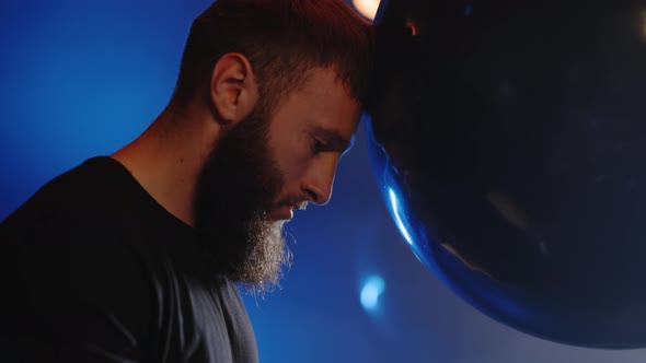 Side View of the Tired Male Boxer Rested Her Head on a Punching Bag After Hard Training and is alt
