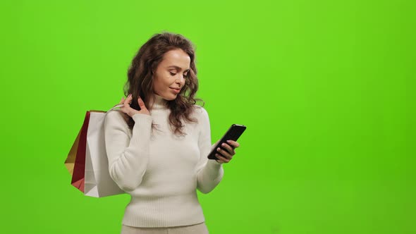 A Woman is Texting on a Smartphone and Holding Shopping Bags in Her Hands alt