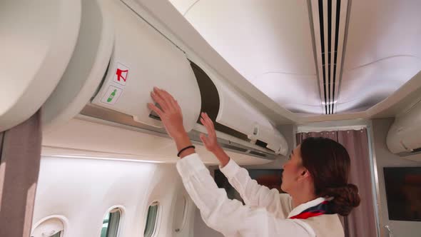 Beautiful flight attendants close luggage compartments overhead on aircraft.