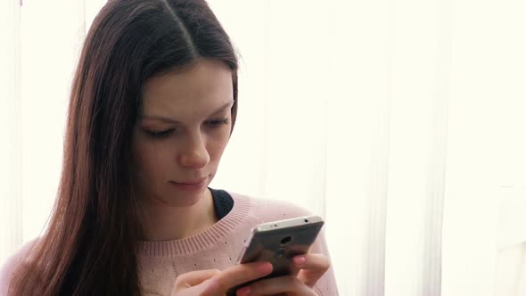 Young Woman Brunette Is Typing a Message on Her Mobile Phone and Looking at Screen.
