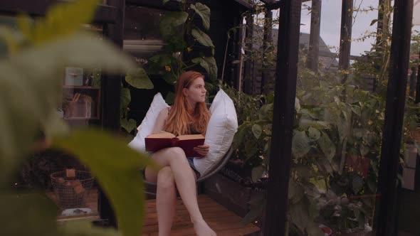 Teenage Girl Sitting On Garden Chair With Pillows And Reading alt