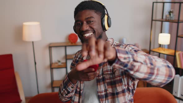 Overjoyed Young Man in Wireless Headphones Dancing Singing on Cozy Couch in Living Room at Home alt