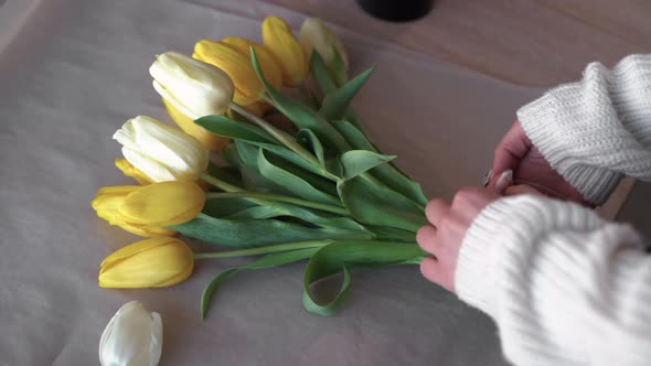 Unrecognizable Woman in a Sweater is Packing a Bouquet of Yellow Tulips alt
