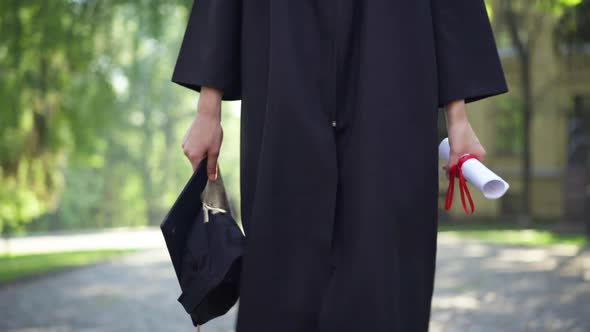 Dolly Shot of Unrecognizable Slim Young Caucasian Woman in Graduation Toga Walking at University alt