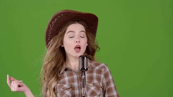 Cowboy Girl in a Leather Hat Sings Into a Retro Microphone. Green Screen. Slow Motion alt