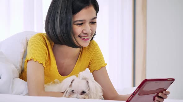 Young woman using tablet in bed with her Maltese dog. alt