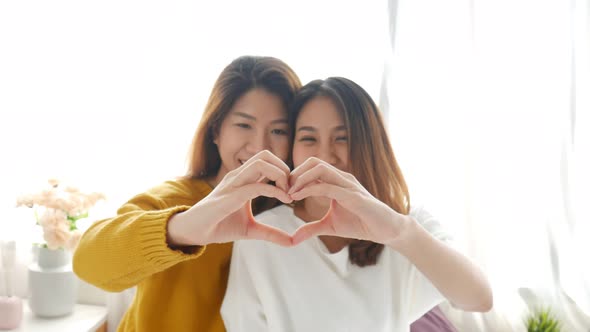 Young Asian lesbian LGBT couple forming a heart shape with a hands-on bedroom at home.