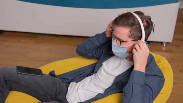 Young Man Listening To Music on Headphones While Is Sitting on a Bean Bag alt