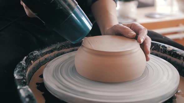 A woman dries a white clay product with a hair dryer on a potter's wheel. Craft, creativity, the pro