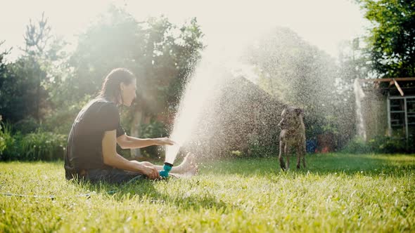 A Young Woman Freshens Up on a Hot Day By Dousing Herself and Her Dog with Water alt