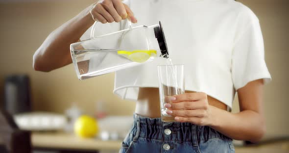 Young Woman Pours Water with Lemon From a Transparent Jug Into a Glass