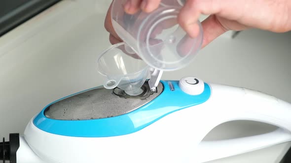 A Man Pours Distilled Water Into a Steam Cleaner Container Using Funnel