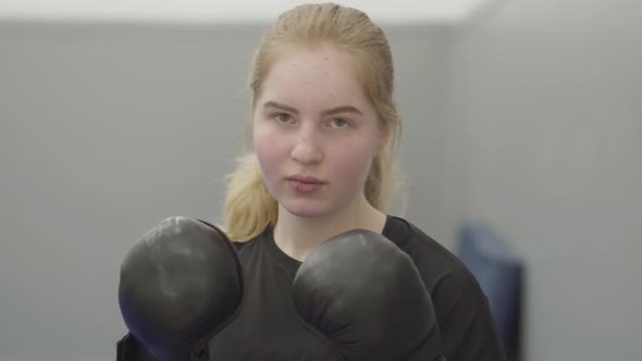 Portrait of Non-confident Blond Woman in Boxing Gloves Imitating Dodging Blows in the Gym Close Up alt