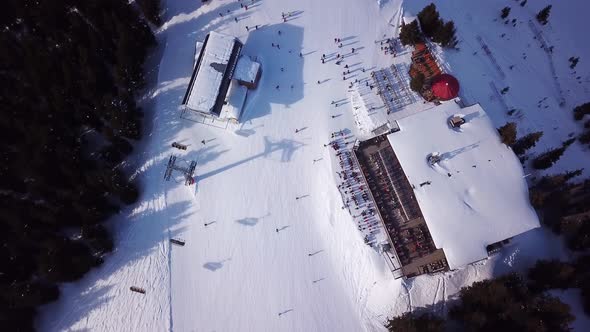 Aerial drone video of crowded ski restaurant with terrace full of people. Apres ski bar surrounded b alt