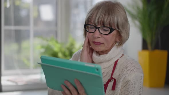 Shocked Caucasian Woman Shaking Head Reading Latest News on Tablet Standing Indoors alt