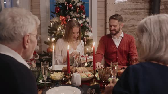 Man Giving Her Wife a Gift at the Table on Christmas Eve Everybody Smiling alt