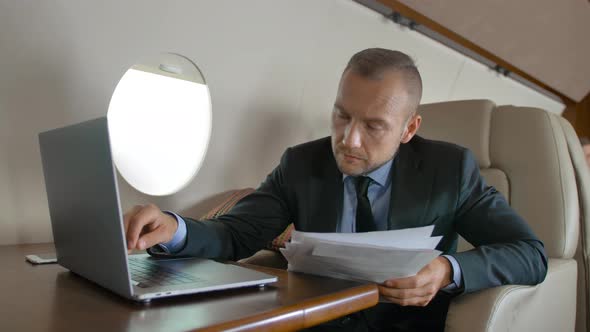 Attractive Businessman Working with Documents and Laptop in Aircraft alt