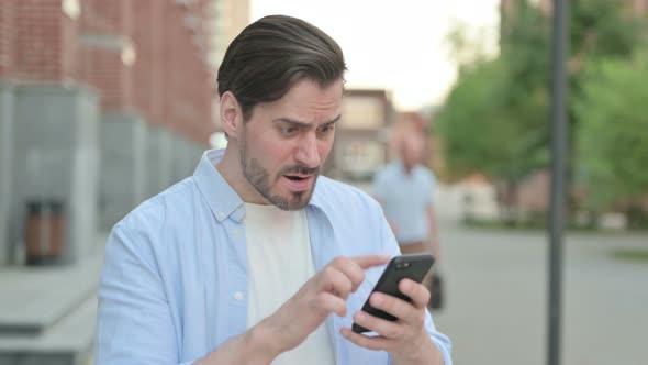 Man Reacting to Loss on Smartphone While Standing Outdoor alt