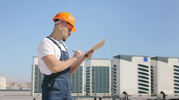 The Young Engineer is Examining the Air Conditioning System and Entering the Data Into the Documents alt