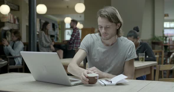 Man using laptop and drinking coffee in pub