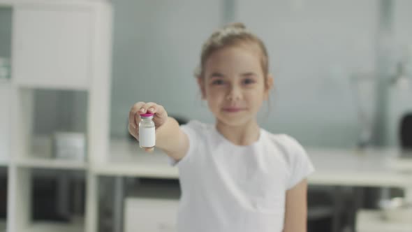 A Cute Girl in a White Tshirt Shows a Bottle of Vaccine to the Camera and Smiles Variable Focus alt
