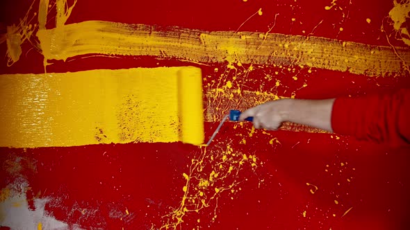 A Man in Hoodie Walking By the Red Wall and Drawing Lines with a Yellow Color Using a Paintint alt