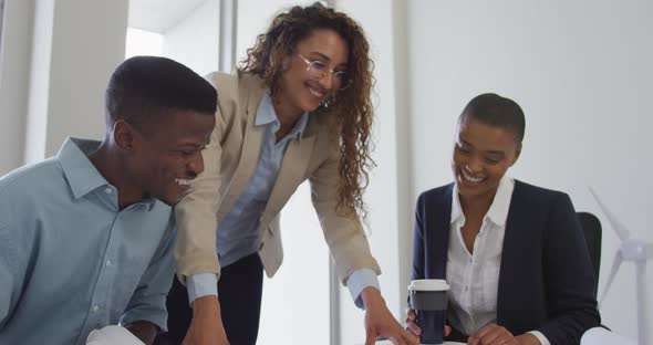 Biracial smiling female and male architects talking and checking architects plans in modern office alt