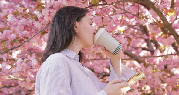 Charming lady drinking coffee and resting in a blooming garden on at sunny day alt